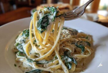 A fork lifts a bite of linguine coated in creamy sauce and spinach from a plate of Creamy Lemon Ricotta Pasta with Spinach.