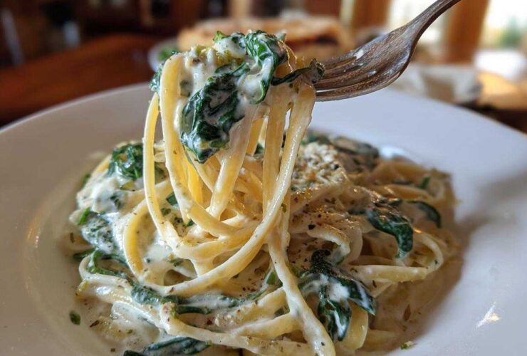 A fork lifts a bite of linguine coated in creamy sauce and spinach from a plate of Creamy Lemon Ricotta Pasta with Spinach.