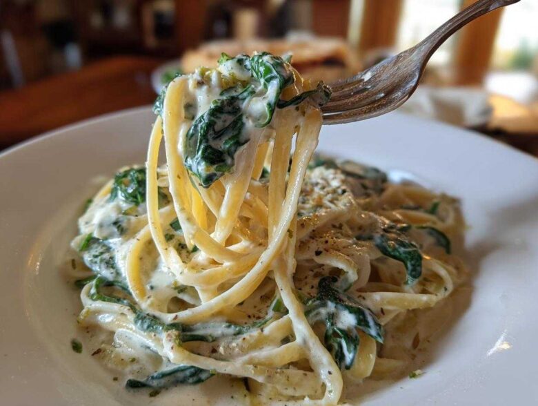 A fork lifts a bite of linguine coated in creamy sauce and spinach from a plate of Creamy Lemon Ricotta Pasta with Spinach.
