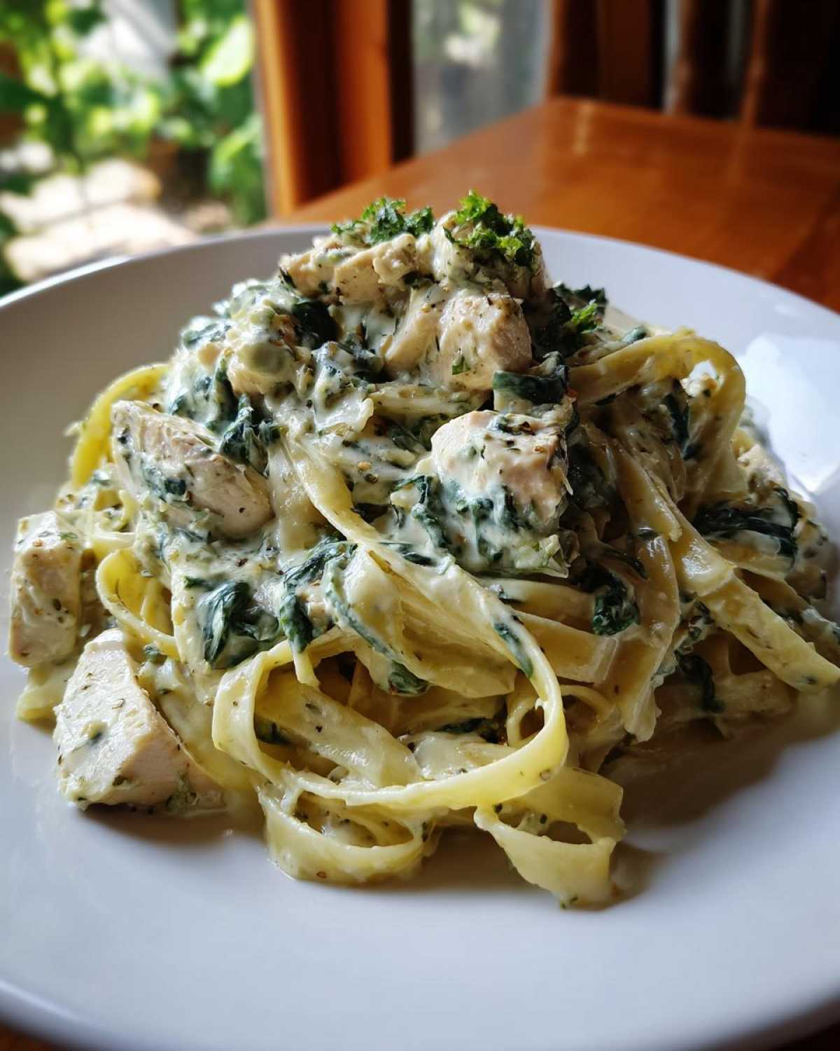 A close-up of Creamy Spinach Pasta with Chicken Dinner featuring fettuccine, chunks of chicken, and spinach in a rich white sauce, garnished with parsley.