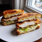 Cross-section view of a thick Crispy Chicken Sandwich with Garlic Sauce, showing golden bread, white chicken, lettuce, and pickles.
