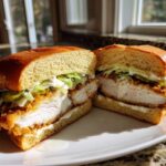 A close-up, halved view of a Crispy Chicken Sandwich with Garlic Sauce, showing thick fried chicken, pickles, lettuce, and sauce on a brioche bun.