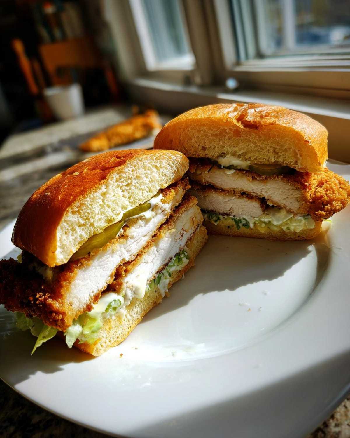 A Crispy Chicken Sandwich with Garlic Sauce cut in half, showing thick fried chicken, pickles, and sauce on a brioche bun.