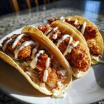 Three Crispy Chicken Tacos filled with shredded lettuce and drizzled generously with a white garlic lime sauce.