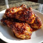 Four glossy, caramelized Crispy Honey Garlic Chicken Drumsticks Oven Baked piled on a white plate.