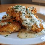 Two golden Crispy Parmesan Chicken Cutlets generously topped with a creamy sauce and fresh parsley.