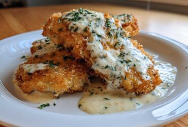 Two golden Crispy Parmesan Chicken Cutlets generously topped with a creamy sauce and fresh parsley.