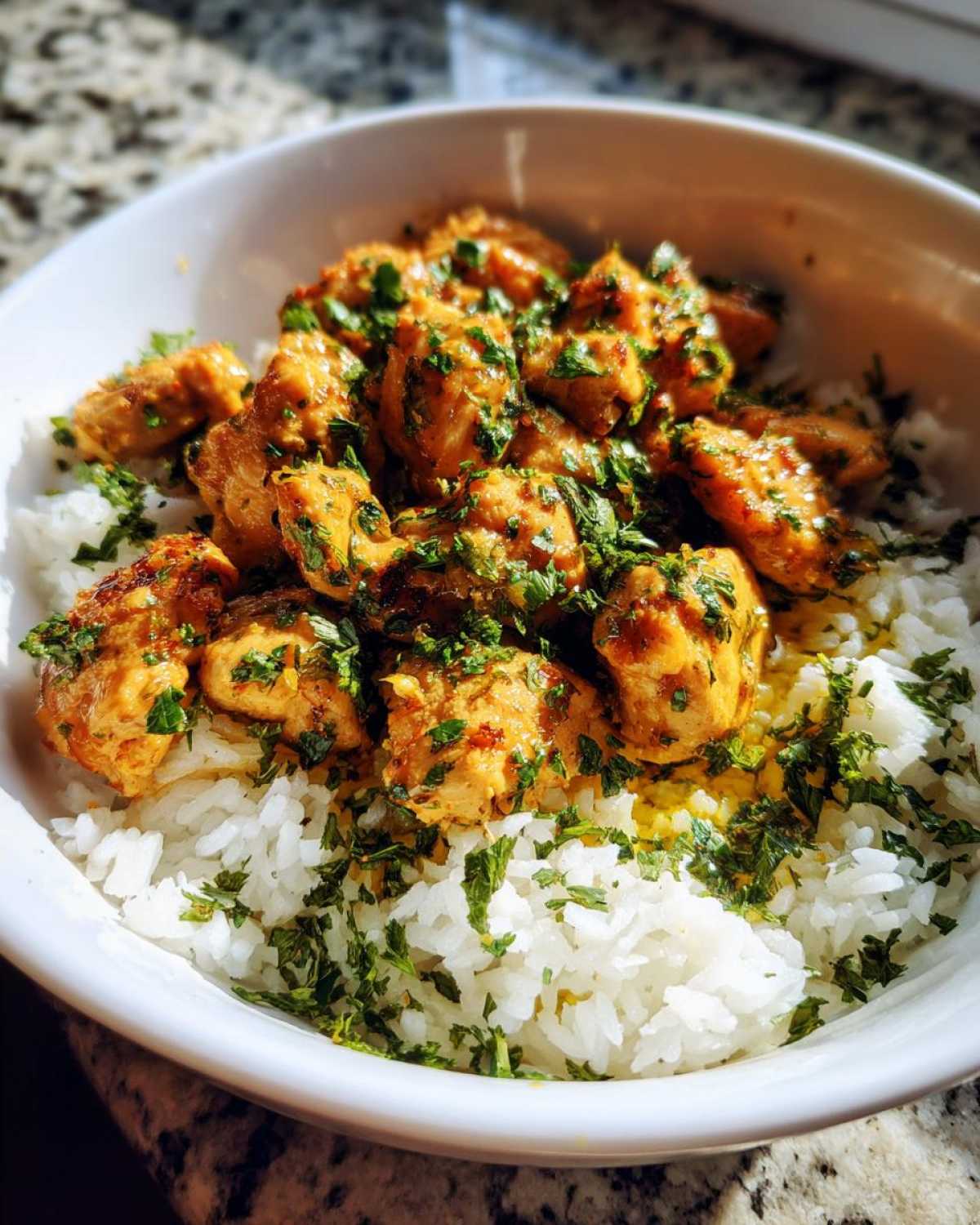 Close-up of Garlic Butter Chicken and Rice dinner served in a white bowl, topped with fresh parsley.