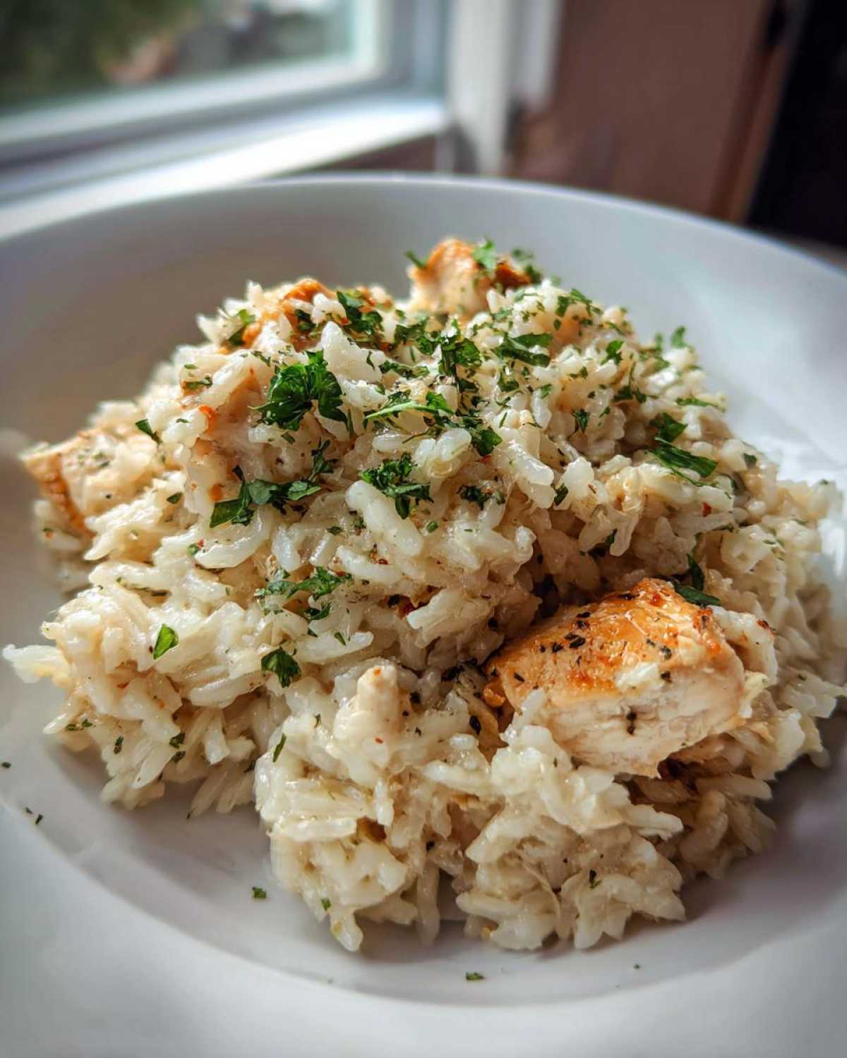 A close-up of Garlic Butter Rice with Chicken Skillet, topped with fresh parsley, served in a white bowl.