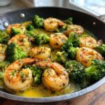 Close-up of juicy shrimp and bright green broccoli florets simmering in rich garlic butter sauce in a skillet.