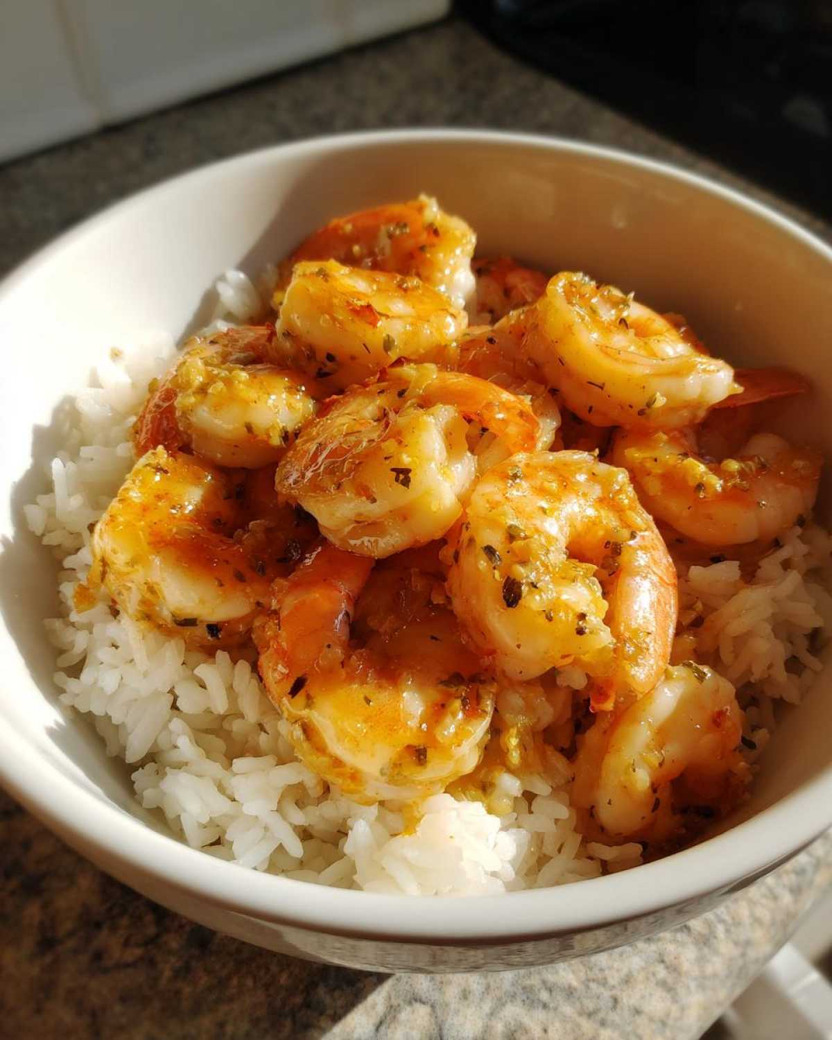 Close-up of a white bowl filled with white rice topped generously with glistening Garlic Butter Shrimp with herbs.