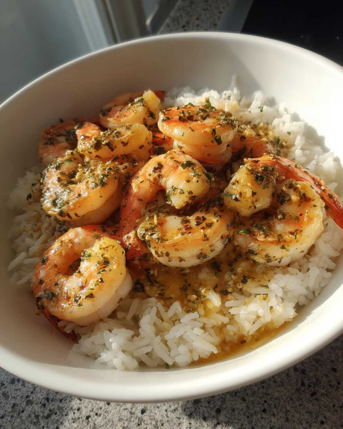 A white bowl filled with white rice topped generously with succulent Garlic Butter Shrimp Bowl with Rice, glistening with sauce and herbs.
