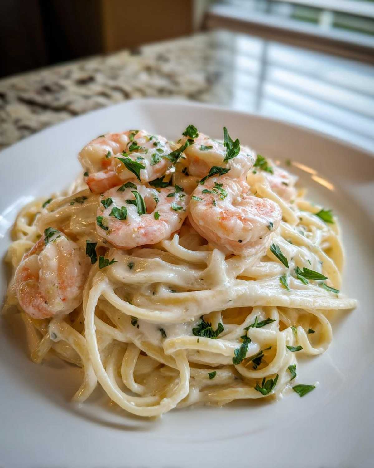 A close-up of Garlic Butter Shrimp Pasta with Cream Sauce, topped with pink shrimp and fresh parsley.