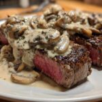Two perfectly cooked steaks topped generously with creamy mushroom sauce, showcasing a medium-rare center of the Garlic Butter Steak.