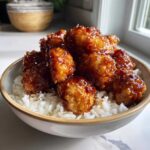 A bowl filled with white rice topped with crispy Honey Garlic Chicken Bites coated in a thick, shiny glaze.