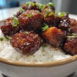 Close-up of glossy Honey Garlic Chicken Bites piled high over fluffy white rice and garnished with green onions.