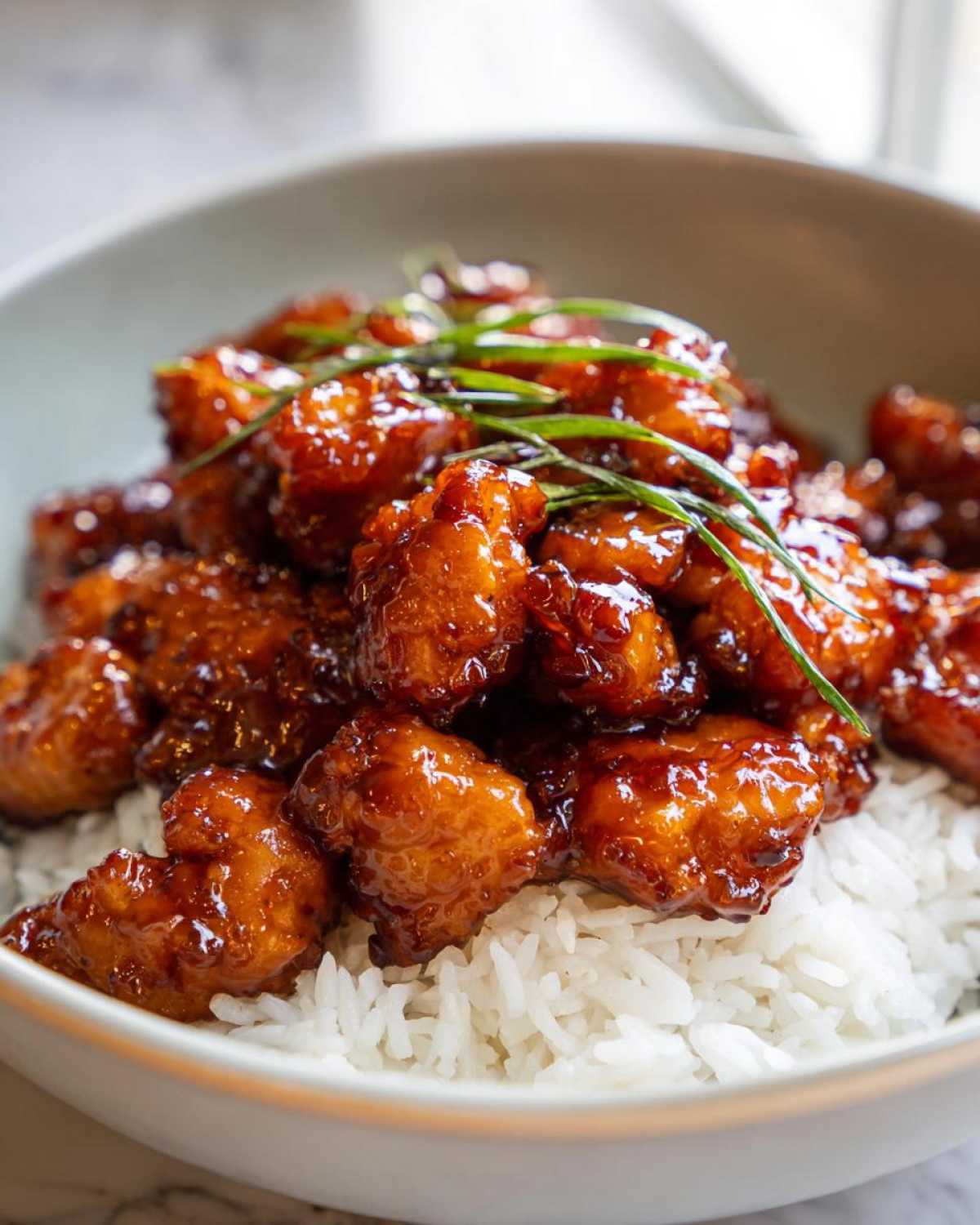 Close-up of glossy Honey Garlic Chicken Bites piled high over a bed of white rice, garnished with green onions.