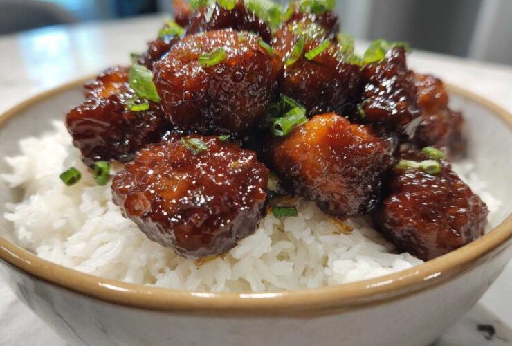 Close-up of glossy Honey Garlic Chicken Bites piled high over fluffy white rice and garnished with green onions.
