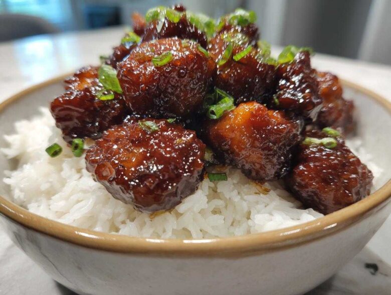Close-up of glossy Honey Garlic Chicken Bites piled high over fluffy white rice and garnished with green onions.