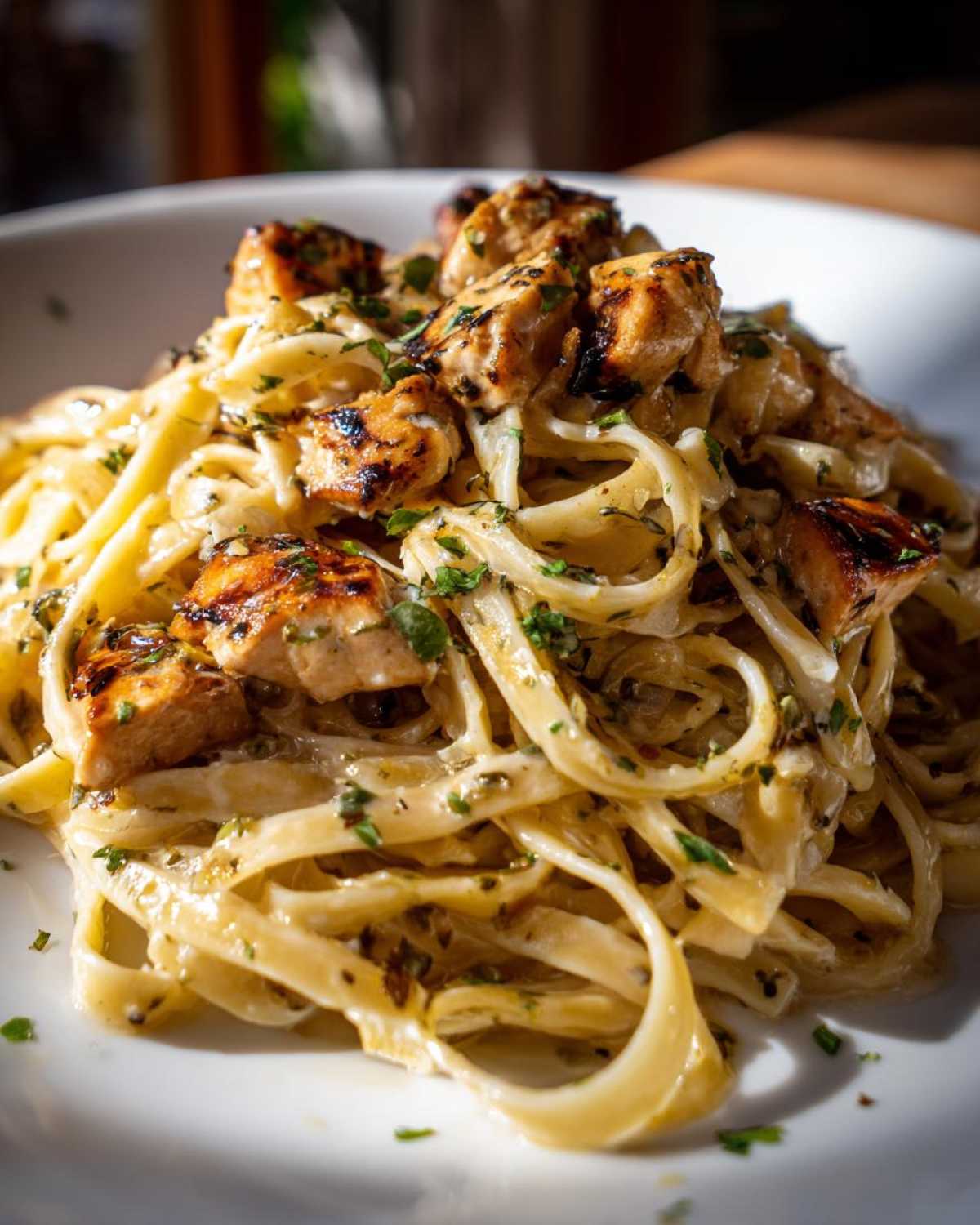 A close-up of fettuccine pasta coated in a creamy sauce, topped with grilled chunks of Honey Garlic Chicken Pasta with Cream Sauce and fresh parsley.
