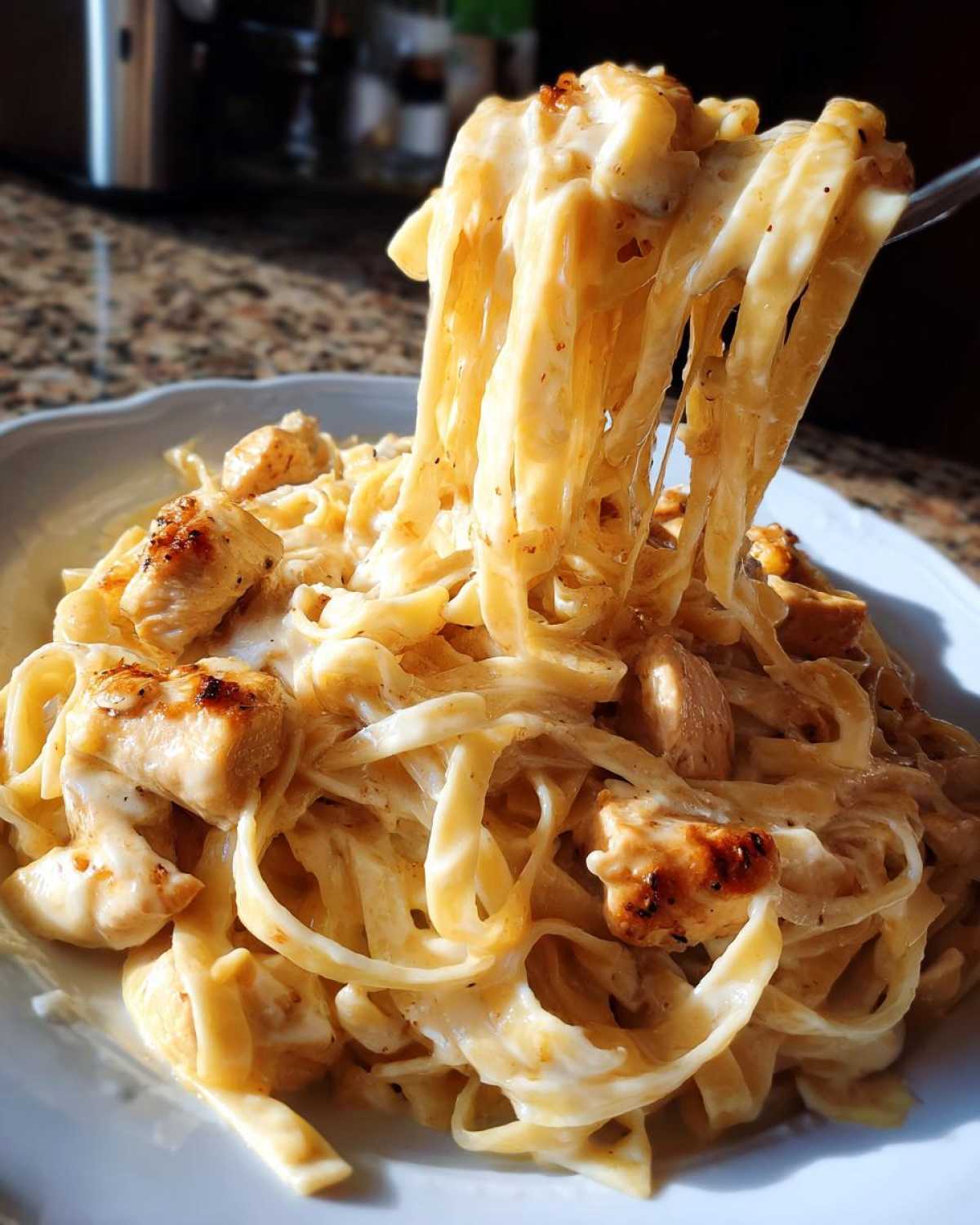 A fork lifting a generous portion of creamy Honey Garlic Chicken Pasta, showing coated fettuccine noodles and browned chicken pieces.