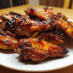 A pile of glossy, sticky Honey Garlic Chicken Wings Oven Baked, caramelized and slightly charred, served on a white plate.