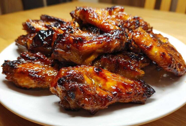 A pile of glossy, sticky Honey Garlic Chicken Wings Oven Baked, caramelized and slightly charred, served on a white plate.