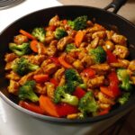 Close-up of Honey Soy Chicken Skillet with Veggies, featuring glazed chicken pieces, bright broccoli florets, carrots, and red peppers.