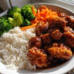 A close-up of a Honey Sriracha Chicken Bowl featuring glazed chicken pieces, white rice, steamed broccoli, and shredded carrots.