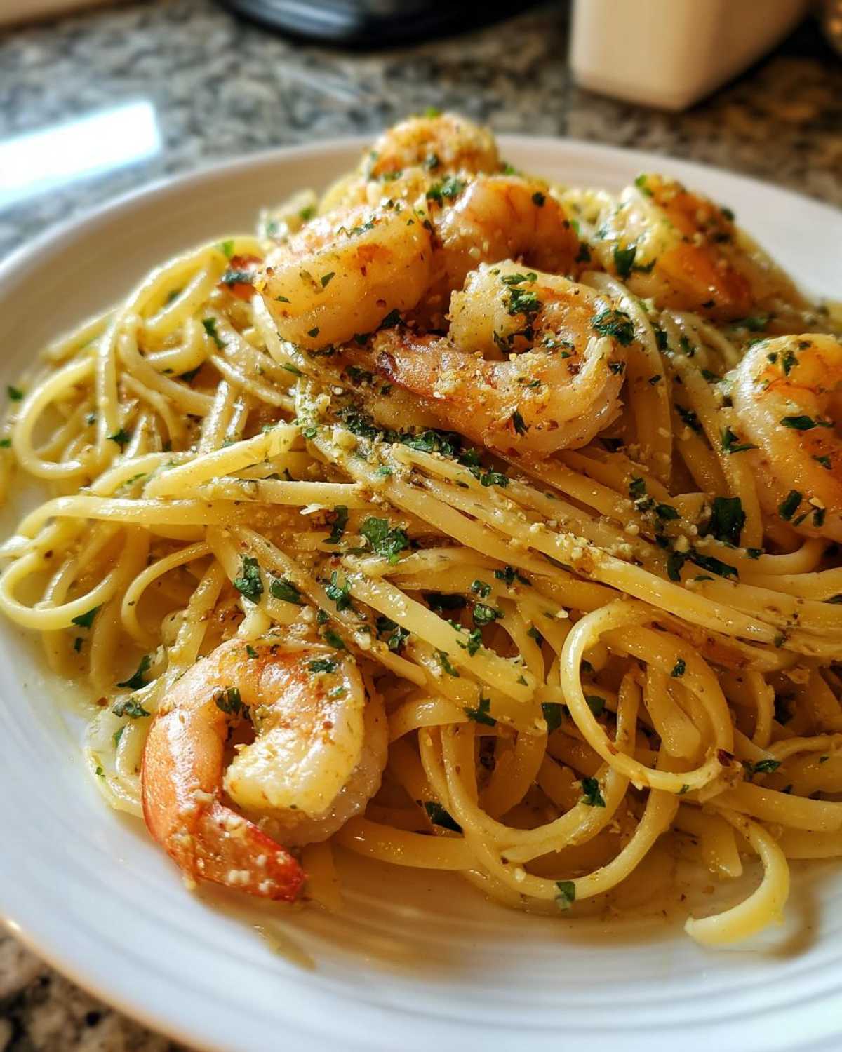 A close-up of a white plate filled with Lemon Butter Shrimp Pasta Ready in 20 Minutes, topped with sautéed shrimp and fresh parsley.