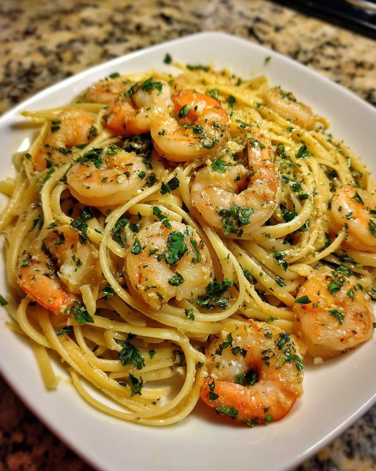 A close-up of a white plate piled high with Lemon Butter Shrimp Pasta Ready in 20 Minutes, topped with large shrimp and parsley.