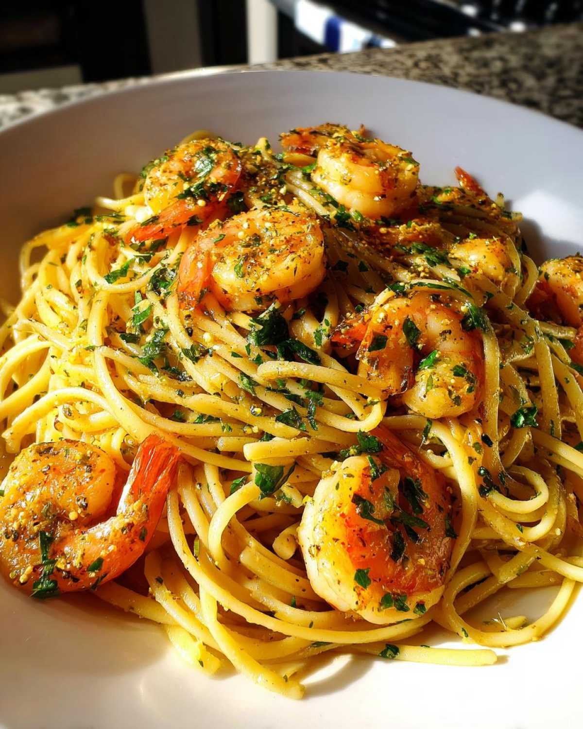 A close-up of a white bowl filled with Lemon Butter Shrimp Pasta, topped with seasoned shrimp and fresh parsley.