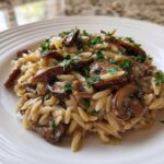 Close-up of a serving of One-Pot Creamy Mushroom Orzo topped with fresh parsley on a white ridged plate.