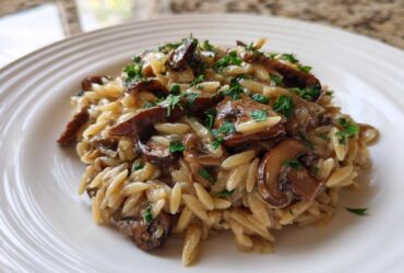 Close-up of a serving of One-Pot Creamy Mushroom Orzo topped with fresh parsley on a white ridged plate.