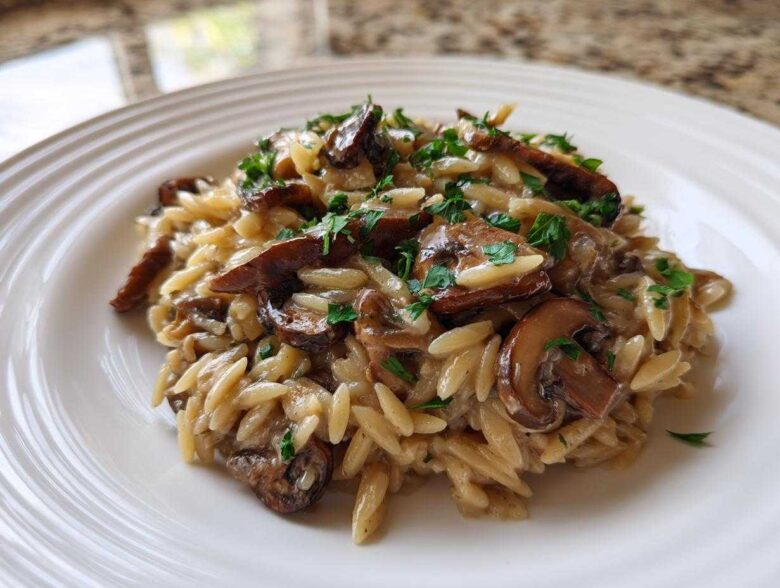 Close-up of a serving of One-Pot Creamy Mushroom Orzo topped with fresh parsley on a white ridged plate.
