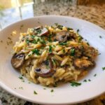A close-up of a white bowl filled with One-Pot Creamy Mushroom Orzo, topped with sautéed mushrooms and fresh parsley.
