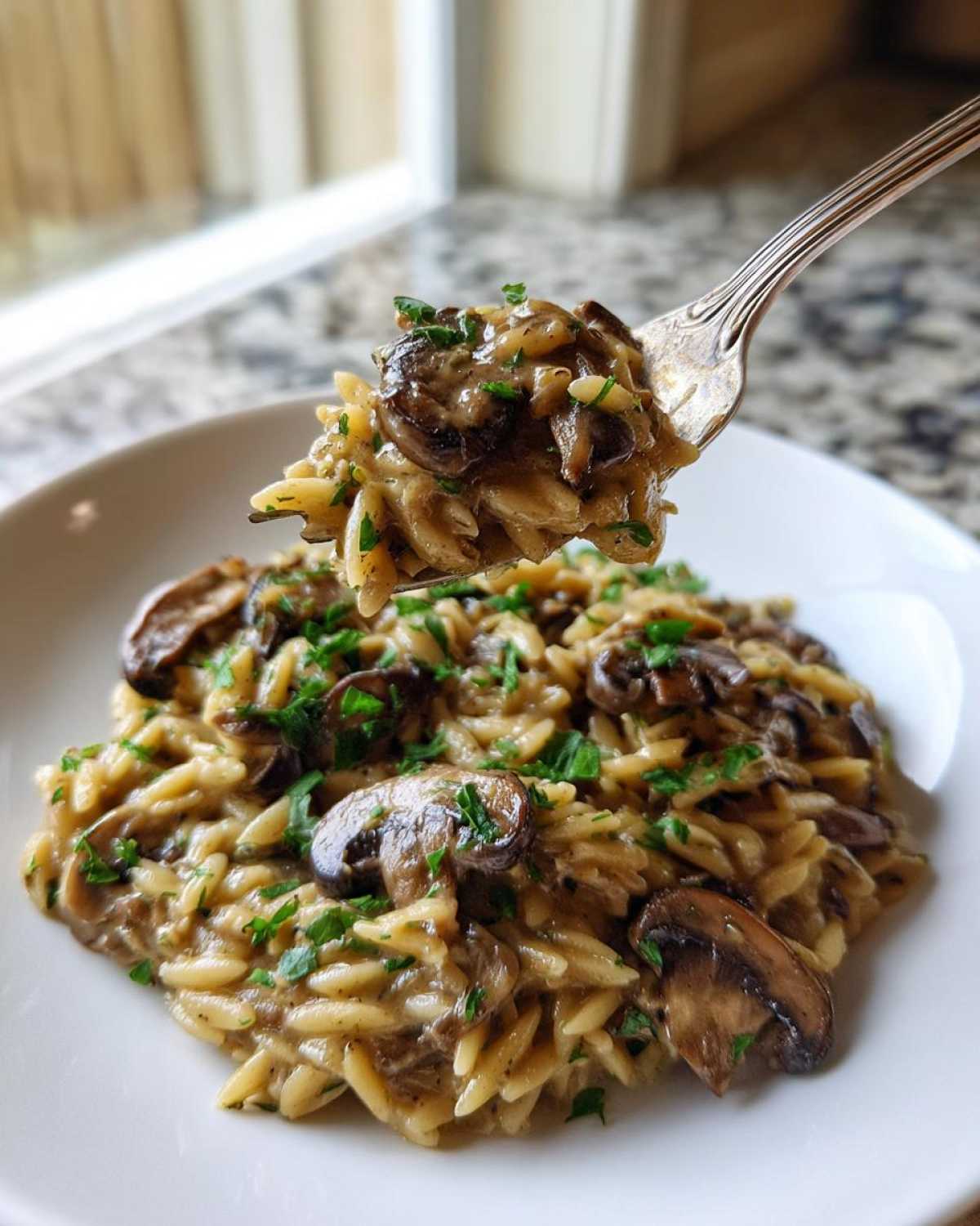 A fork lifting a bite of creamy One-Pot Creamy Mushroom Orzo topped with sautéed mushrooms and fresh parsley.