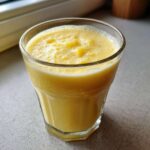A close-up shot of a vibrant yellow Pineapple Coconut Smoothie in a clear glass on a countertop.