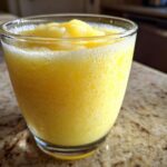 Close-up of a vibrant, icy Pineapple Coconut Smoothie served in a clear glass on a granite countertop.