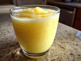 Close-up of a vibrant, icy Pineapple Coconut Smoothie served in a clear glass on a granite countertop.