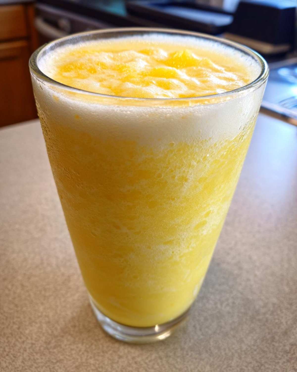 A tall glass filled with a bright yellow, icy Pineapple Coconut Smoothie, showing a frothy top layer.