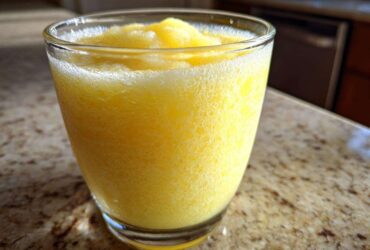 Close-up of a vibrant, icy Pineapple Coconut Smoothie served in a clear glass on a granite countertop.