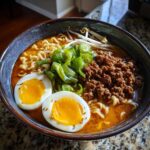 A close-up of Spicy Miso Ramen featuring rich broth, ground meat, scallions, and two halves of a soft-boiled egg.