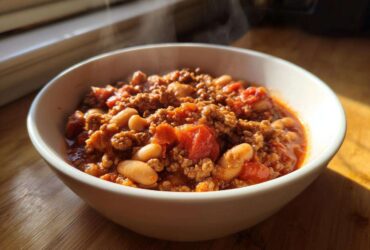 A steaming white bowl filled with rich, thick Spicy Turkey White Bean Chili featuring ground turkey and white beans.