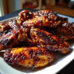 A plate piled high with glistening, caramelized Sticky Honey Garlic Wings Oven Baked, sprinkled with chili flakes.