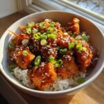 Close-up of a Sticky Orange Chicken Bowl with crispy chicken coated in glaze, served over white rice and topped with sesame seeds and green onions.
