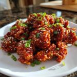Close-up of sticky Sweet Chili Chicken Easy Recipe pieces coated in glossy sauce, topped with sesame seeds and green onions.