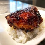 Close-up of a glazed Sticky Sweet Chili Chicken Thighs resting on a bed of white rice.