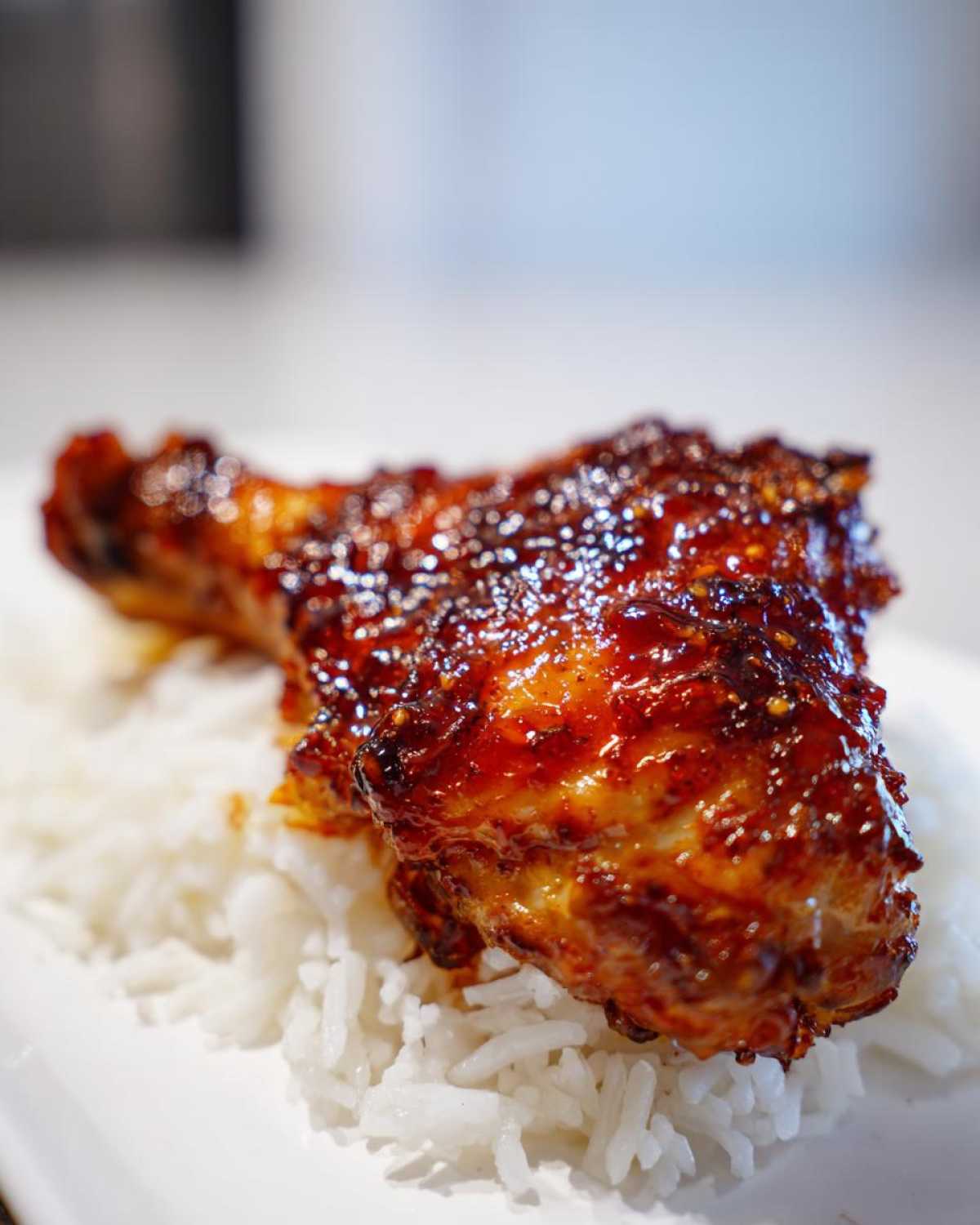 Close-up of a glazed chicken thigh resting on a bed of white rice, featuring the sticky sweet chili chicken thighs recipe.