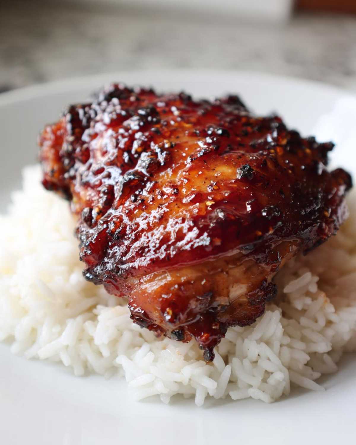 Close-up of a glazed Sticky Sweet Chili Chicken Thighs resting on a bed of fluffy white rice.